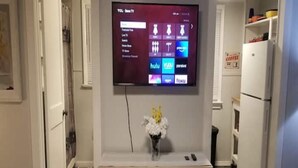 Une cuisine moderne avec un téléviseur à écran plat fixé au mur, une console en bois ornée d’un vase de fleurs et une cheminée intégrée.