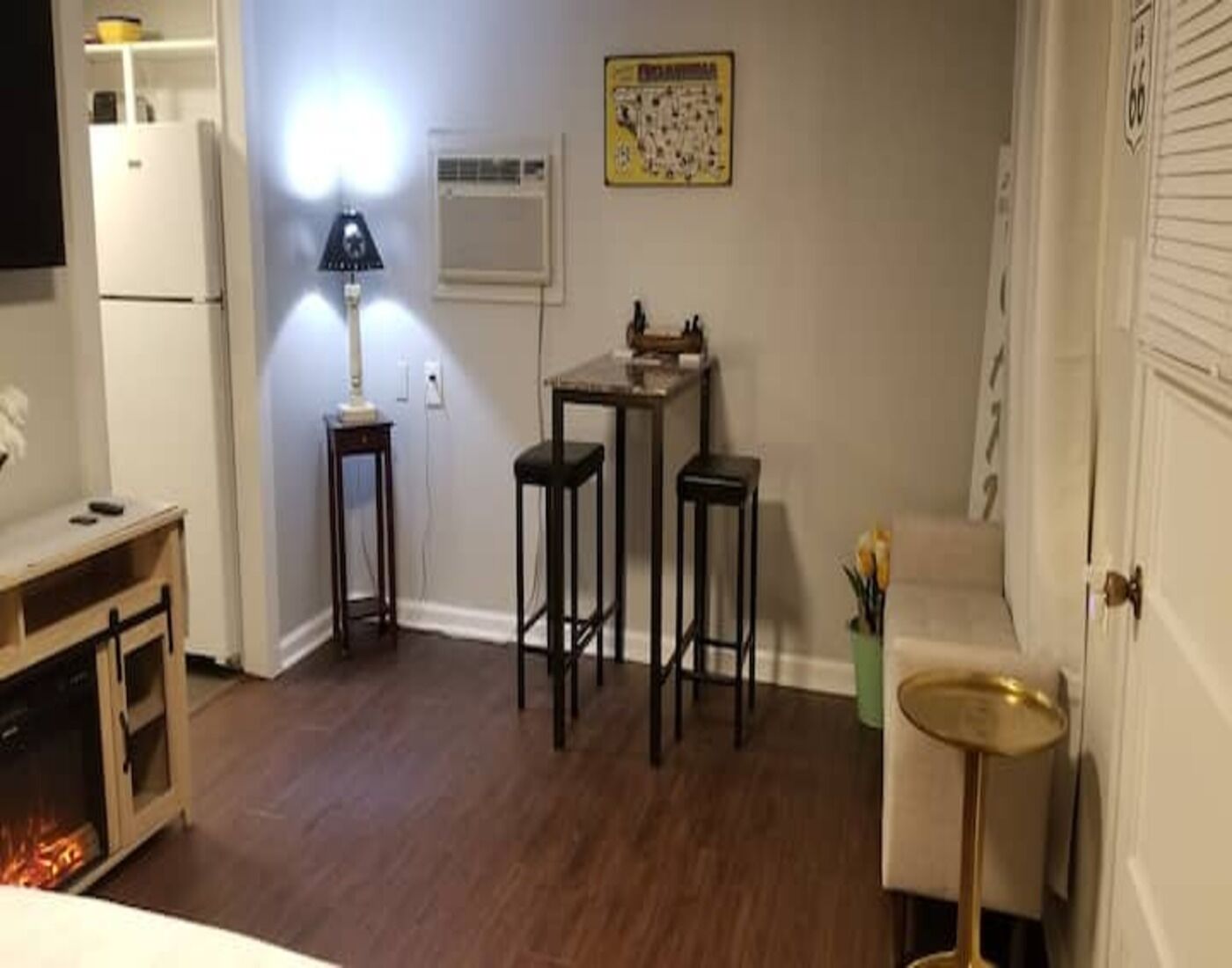 A compact living space with a kitchenette, a dining area with stools, a small table, and a decorative lamp.