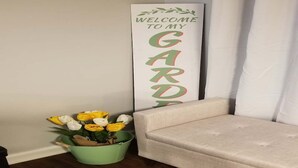 Une pancarte accueillante à l’entrée d’un jardin, un seau vert rempli de fleurs et un canapé beige.