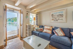 Une pièce avec un canapé bleu, une table basse blanche, une porte donnant sur un balcon et un tableau encadré au mur.
