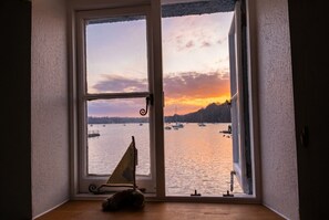Ett rum med ett fönster som vetter mot en sjö eller ett hav, och där man kan se solnedgången. I rummet finns också en liten modell av en segelbåt och ett trägolv.