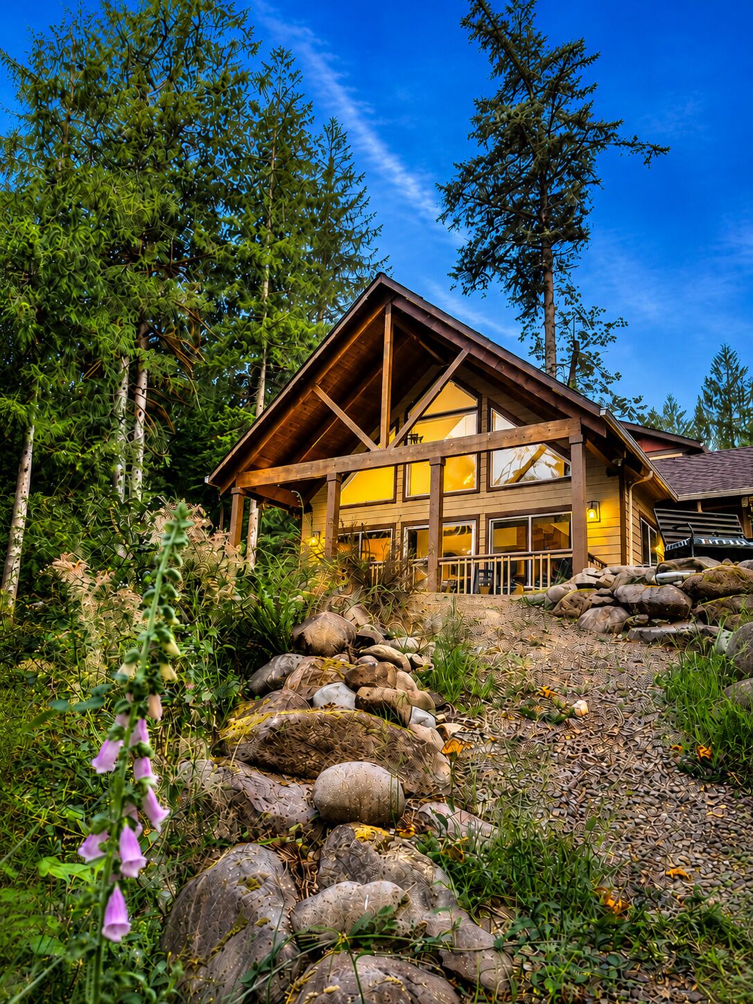 Une cabane en bois dotée d’une grande fenêtre, entourée de rochers et de verdure.