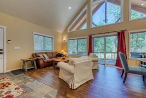 Relax in this spacious living area with a high ceiling and large windows, featuring a comfortable sofa set, armchair, and dining table.