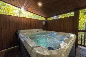 A hot tub in a wooden cabin with a wooden deck and a view of trees. - New Cabin w Hot Tub, Covered Deck, Fire Pit & Games - Morning Primrose (broken bow)