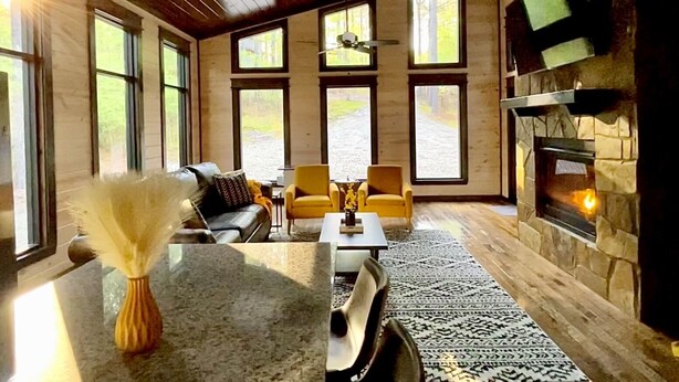 A spacious living room with large windows, a stone fireplace, and a modern seating area.