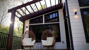 A modern house with a covered porch, two wicker chairs, and a large window.