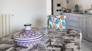 Une pièce avec une table recouverte d’une nappe à motifs de journal, un pot en céramique décoratif et une chaise à motifs colorés.