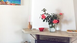 Un salon avec une cheminée, un tableau accroché au mur et un vase rempli de fleurs posé sur la cheminée.