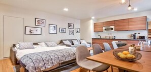 Quarto de hotel moderno com uma cama, uma mesa de jantar com cadeiras, uma cozinha e quadros nas paredes.