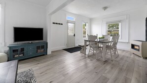A spacious living room with a flat-screen TV, a dining table with chairs, and a fireplace.