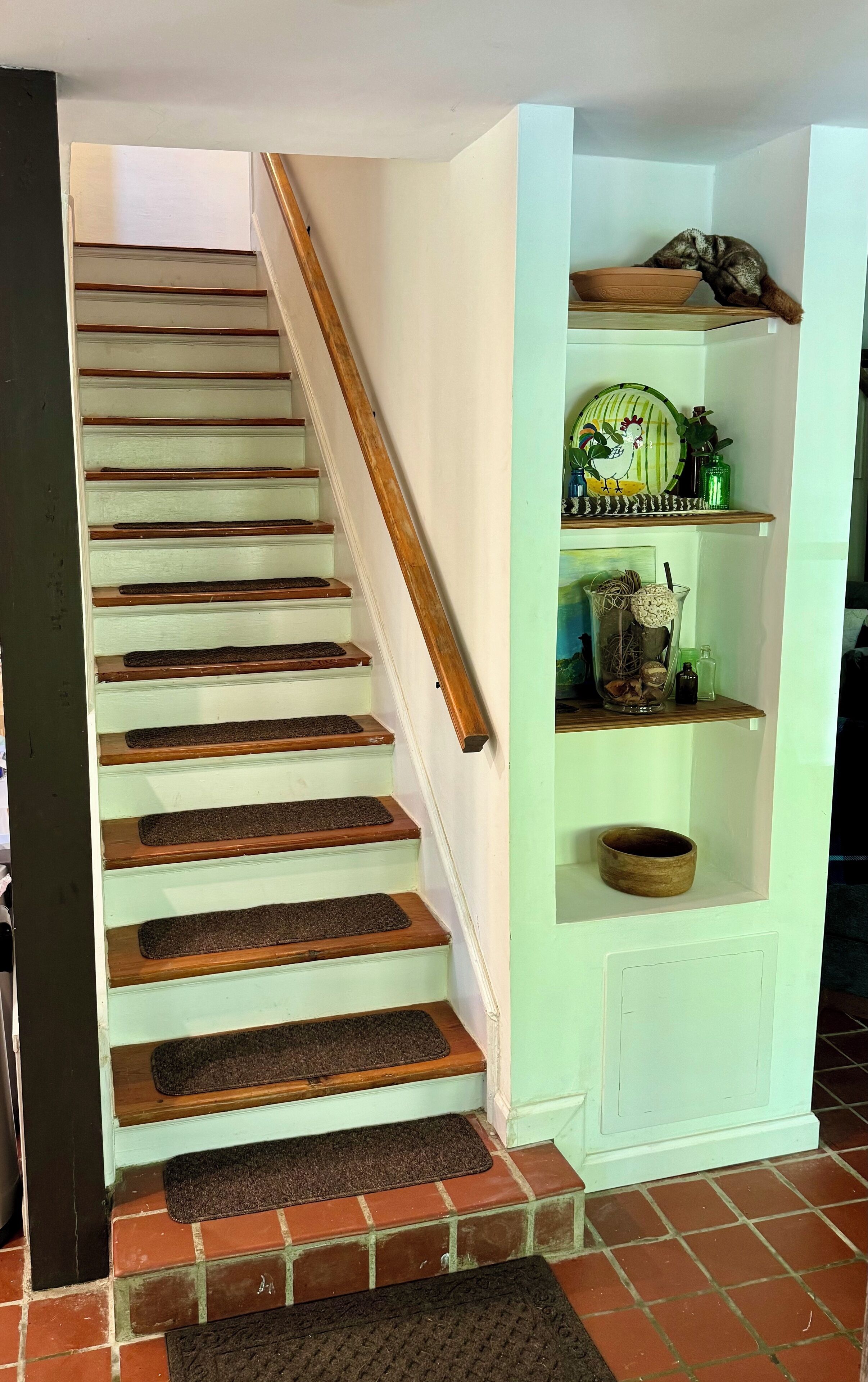 A staircase with wooden steps and a handrail, leading to a landing with a shelf holding decorative items.