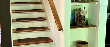 A staircase with wooden steps and a handrail, leading to a landing with a shelf holding decorative items.
