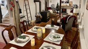 Ein Essbereich mit einem Holztisch, gedeckt für vier Personen, umgeben von Stühlen. Im Hintergrund sind ein Weihnachtsbaum und ein Kamin erkennbar.