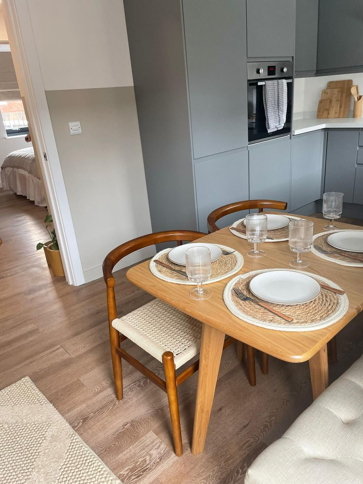 A dining area with a wooden table set for four, surrounded by chairs with woven seats.
