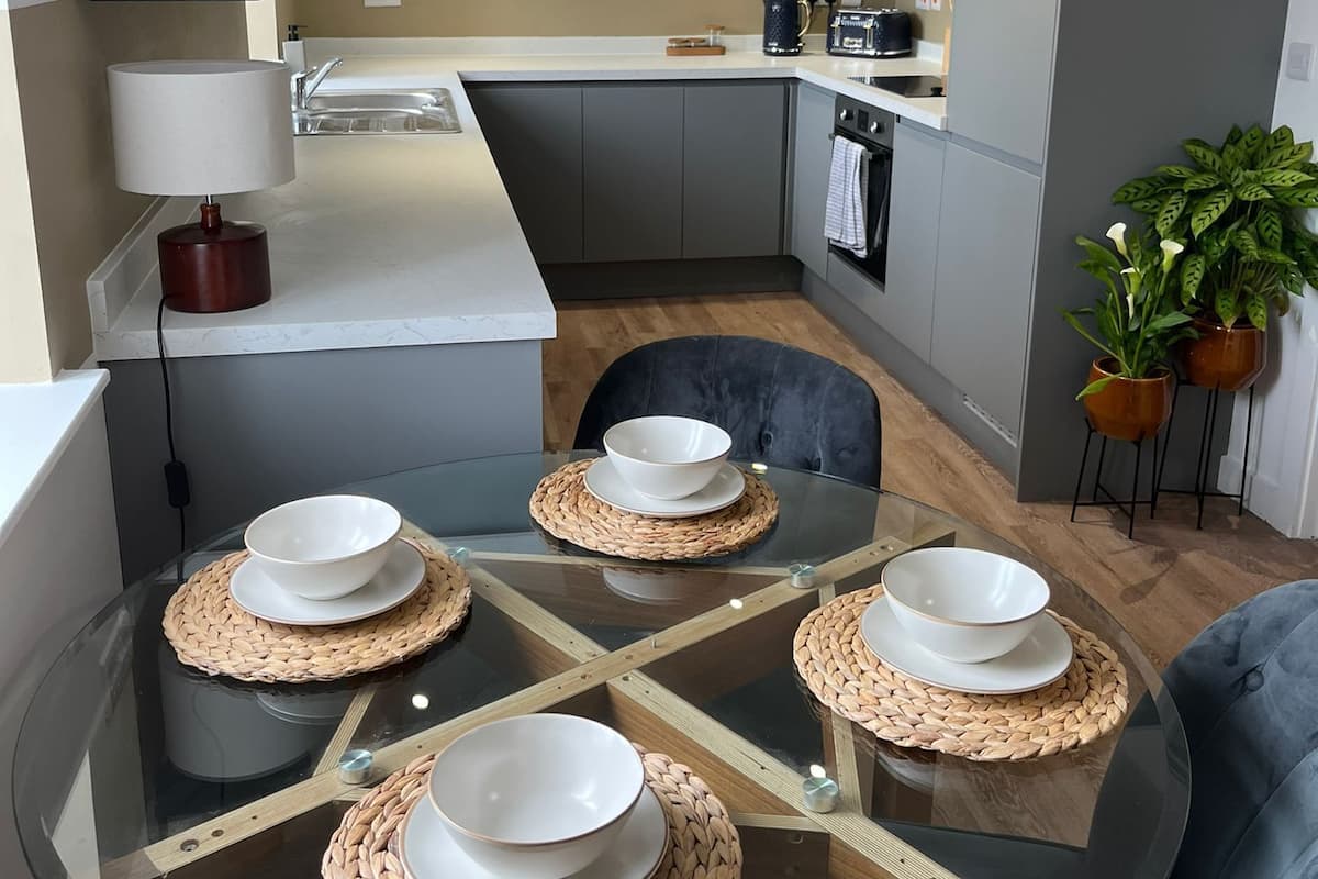 Une cuisine moderne avec une table à manger en verre pour quatre personnes, une machine à café et une plante.