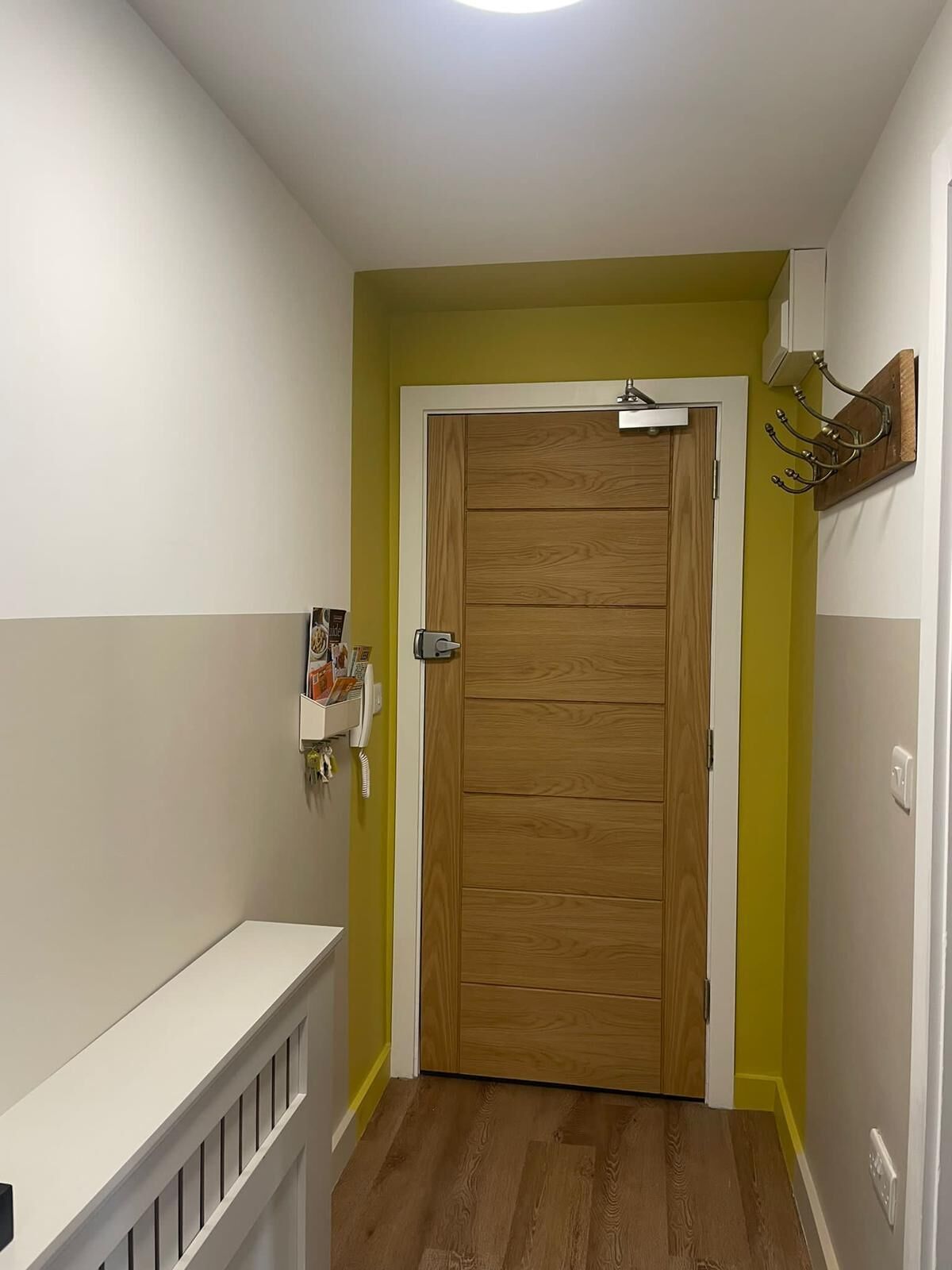 Een hal met een houten deur, een witte console tafel en een telefoon aan de muur.