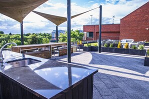 Une terrasse sur le toit équipée d’un évier, de bancs en bois et d’un espace barbecue.