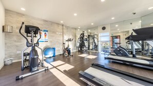 Un gimnasio moderno con diverso equipo de ejercicio, incluyendo cintas de correr y bicicletas estáticas, y un espejo grande que refleja el espacio.
