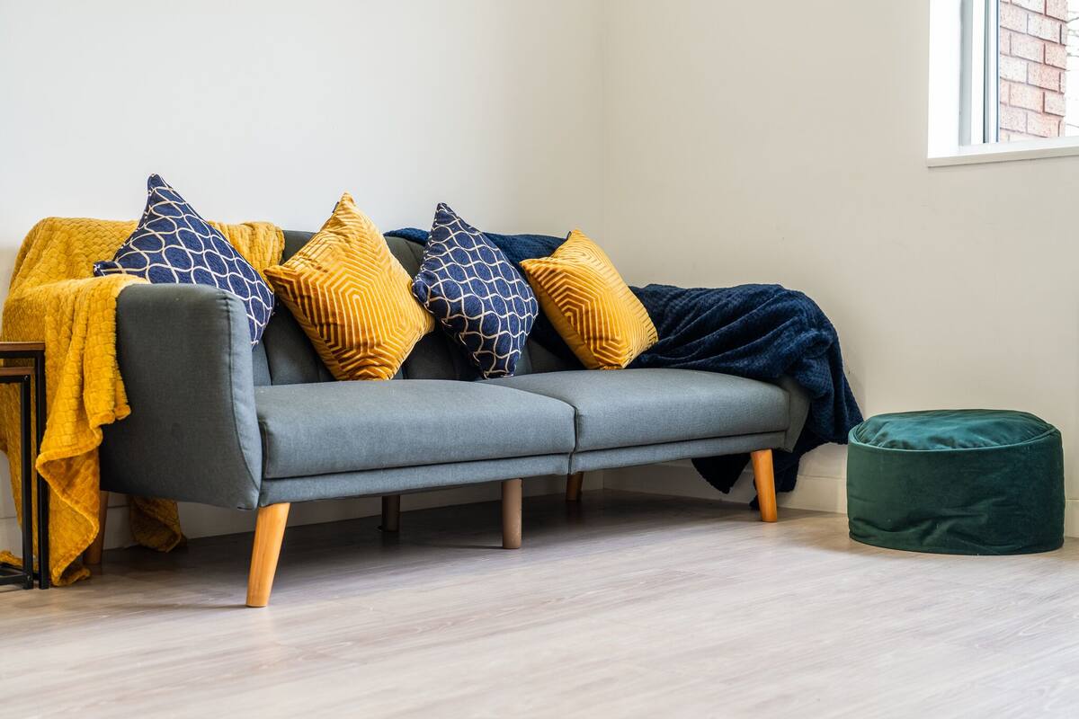 Un sofá gris con cojines estampados y un puf verde en una habitación con suelo de madera clara.