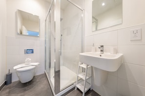 Un baño moderno con cabina de ducha de vidrio, un lavamanos blanco y un inodoro.