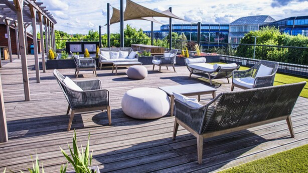 Una terraza al aire libre con mobiliario de mimbre, una mesa redonda grande y una estructura de pérgola.