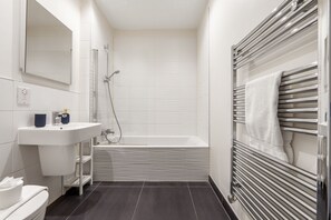 Une salle de bain moderne avec un lavabo blanc, un miroir et une douche dotée d’une porte en verre.