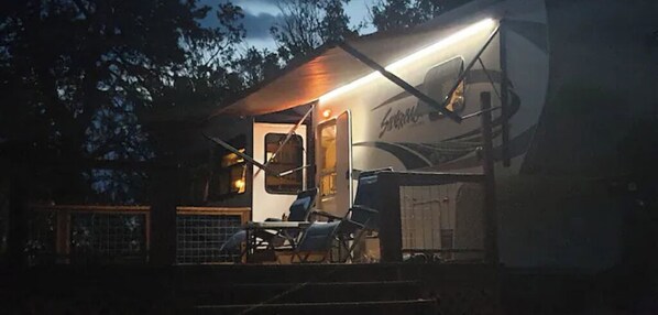 A well-lit RV with a covered porch area, a dining table, and a chair.