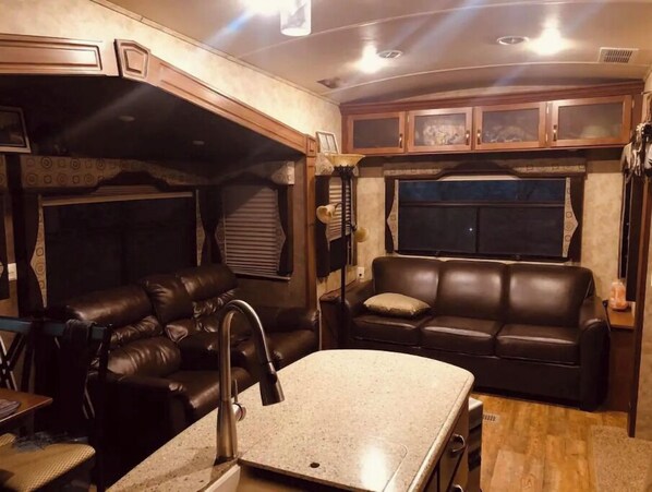 A compact RV interior with a kitchenette, a seating area with a sofa and chairs, and a window.