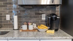 Une cuisine équipée d’un four à micro-ondes, d’une machine à café et d’un saladier rempli de bananes posé sur le comptoir.