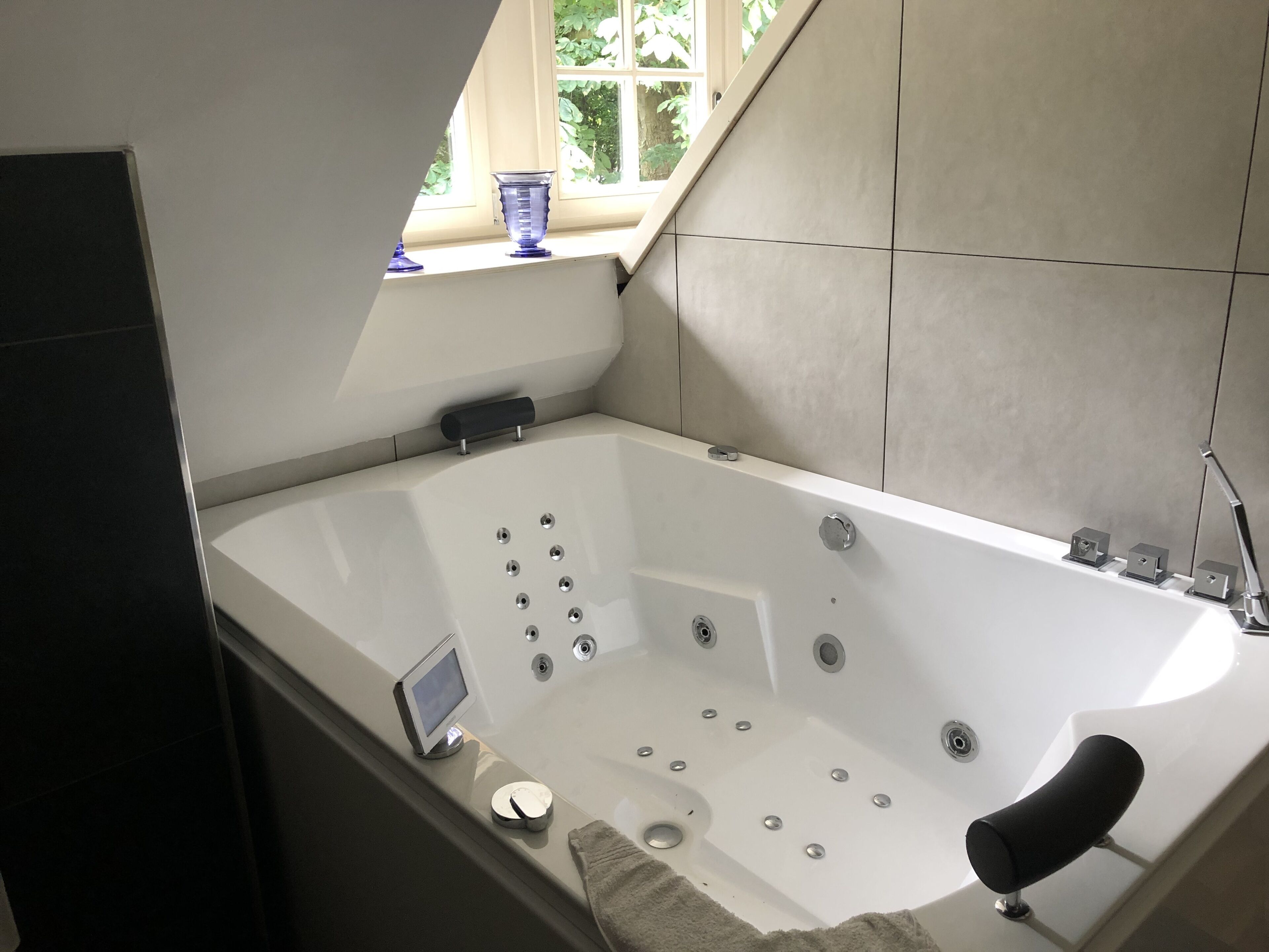 Une salle de bain moderne avec une baignoire sur pieds, une petite fenêtre donnant sur un espace verdoyant et un radiateur encastré.