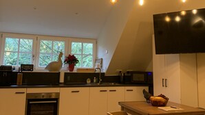 Ett modernt kök med en central köksö, en matplats med bord och stolar samt ett stort fönster som släpper in naturligt ljus.