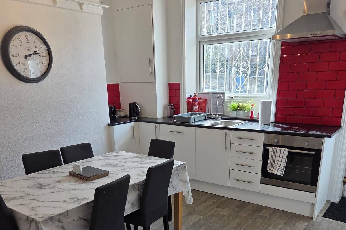 Una cocina compacta con una mesa de comedor, sillas, un reloj y un salpicadero de ladrillo rojo.