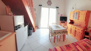 Een kleine kamer met een kitchenette, een eethoek en een bed.