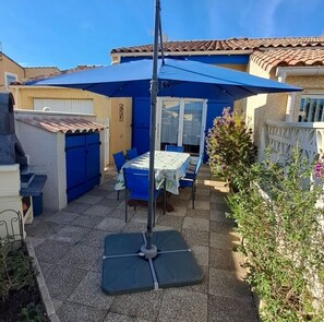 A patio with a table and chairs, a blue umbrella, and a grill. - Vacation home in a residential area near the ocean (Port-la-Nouvelle)
