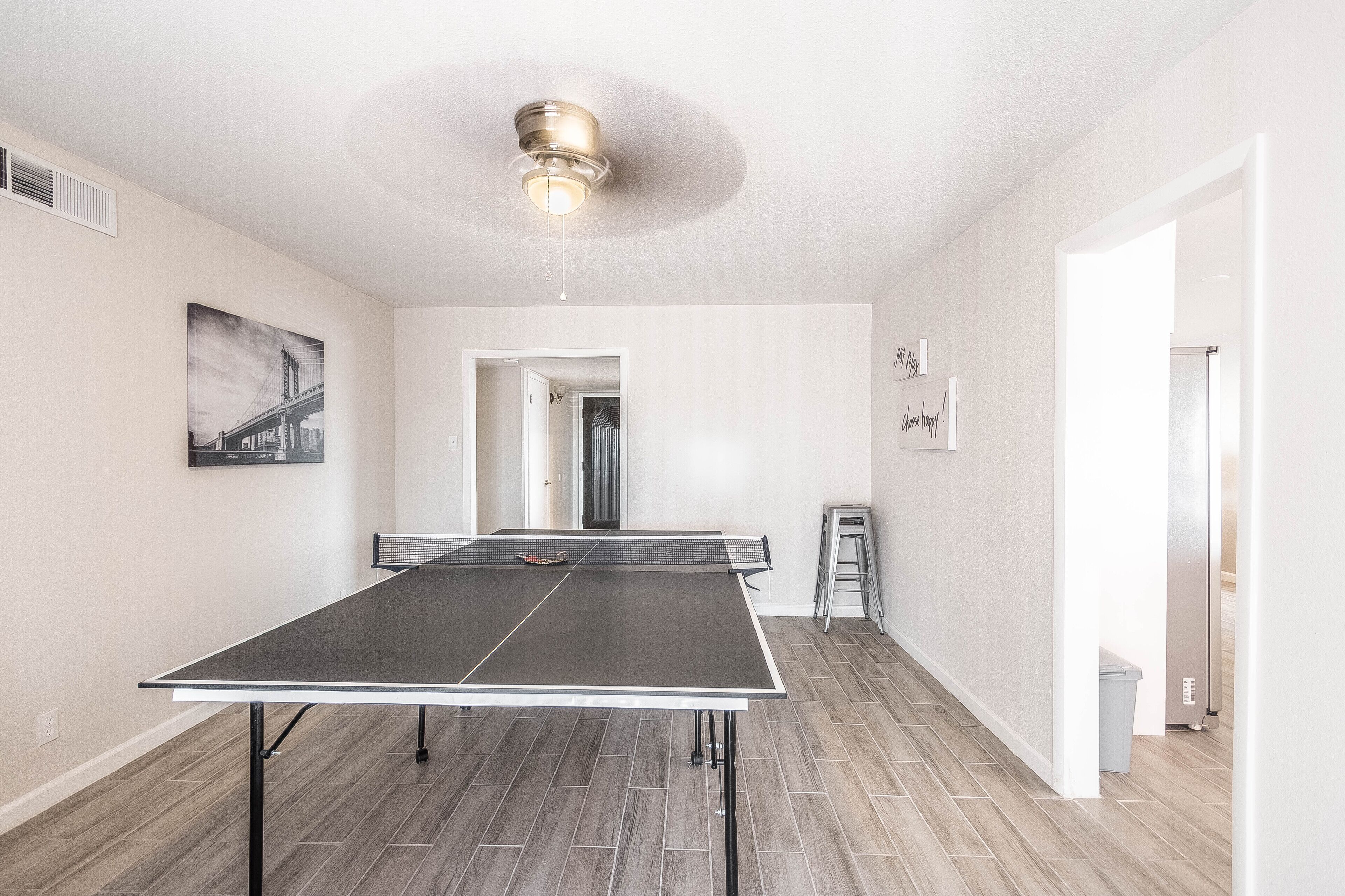 Una habitación con mesa de ping pong, ventilador de techo y puerta que da a otra habitación.