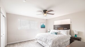 A bedroom with a bed, a ceiling fan, a bedside table with a lamp, and a window with blinds.