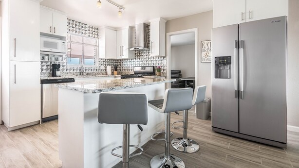 A modern kitchen with white cabinets, a stainless steel refrigerator, and a marble countertop.