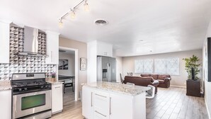 A modern kitchen with a central island, stainless steel appliances, and a dining area with a brown leather couch.