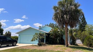 Uma casa térrea com fachada azul clara, uma garagem e uma palmeira grande no quintal da frente.