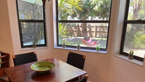 Uma sala de jantar com uma mesa e cadeiras de madeira, uma tigela verde sobre a mesa e janelas com vista para um jardim.