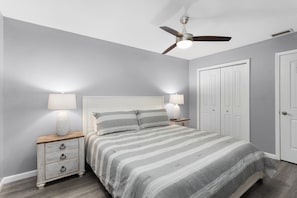 Ein Schlafzimmer mit Bett, Nachttischen, Deckenventilator und einer Tür.