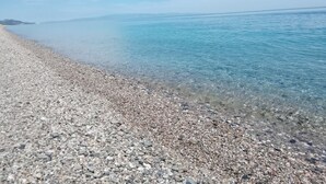 A pebble beach with clear water and a distant shoreline. - Oasi Park Hotel (Mascali)