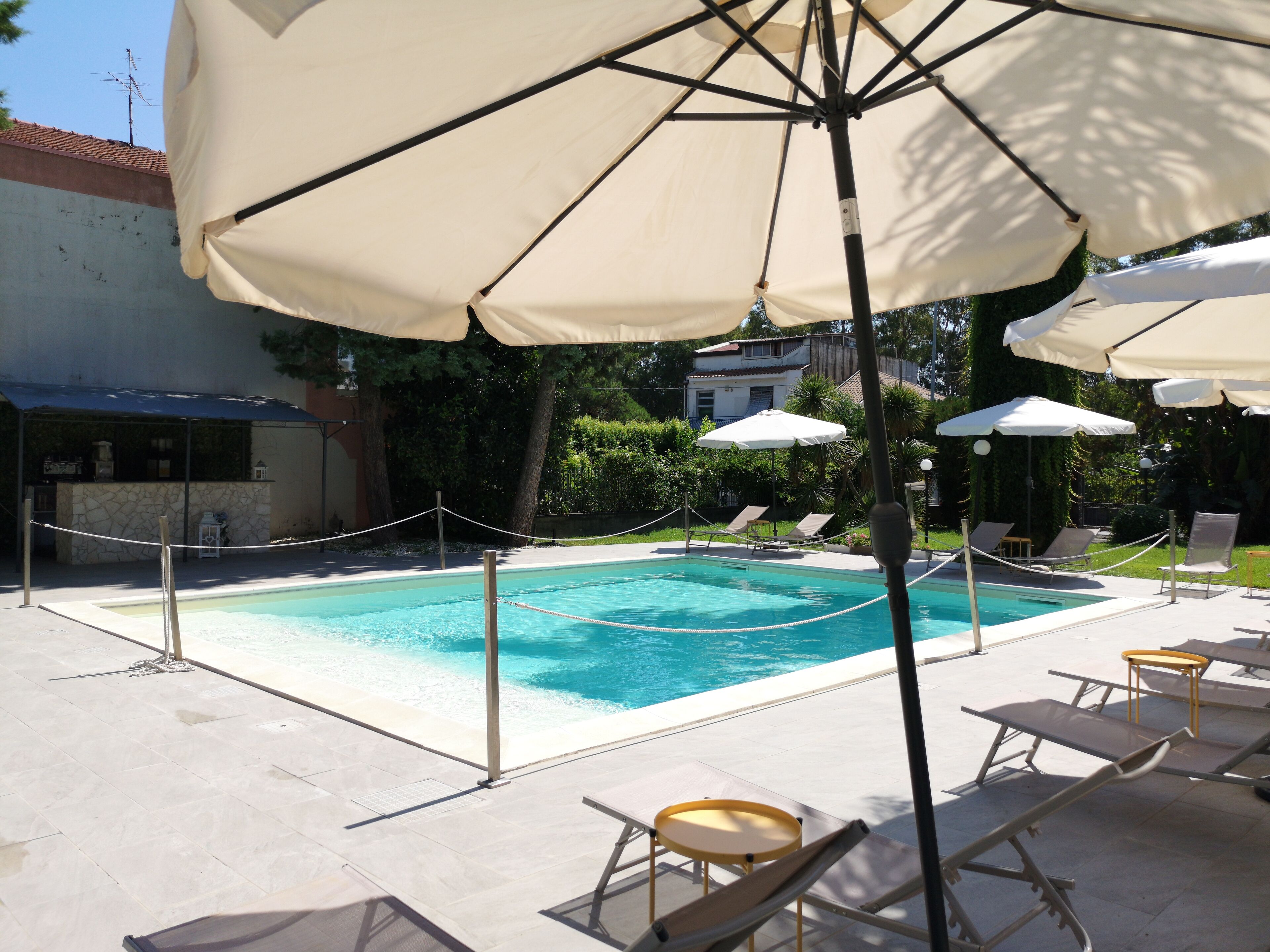 Une piscine entourée d’un mur de pierre et de verdure, avec des chaises longues et des parasols.