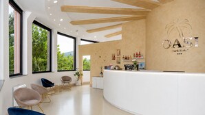 A modern reception area with a curved white counter, a palm tree logo, and a view of greenery through large windows. - Oasi Park Hotel (Mascali)