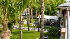 A hotel courtyard with palm trees, outdoor seating, and a covered dining area. - Oasi Park Hotel (Mascali)