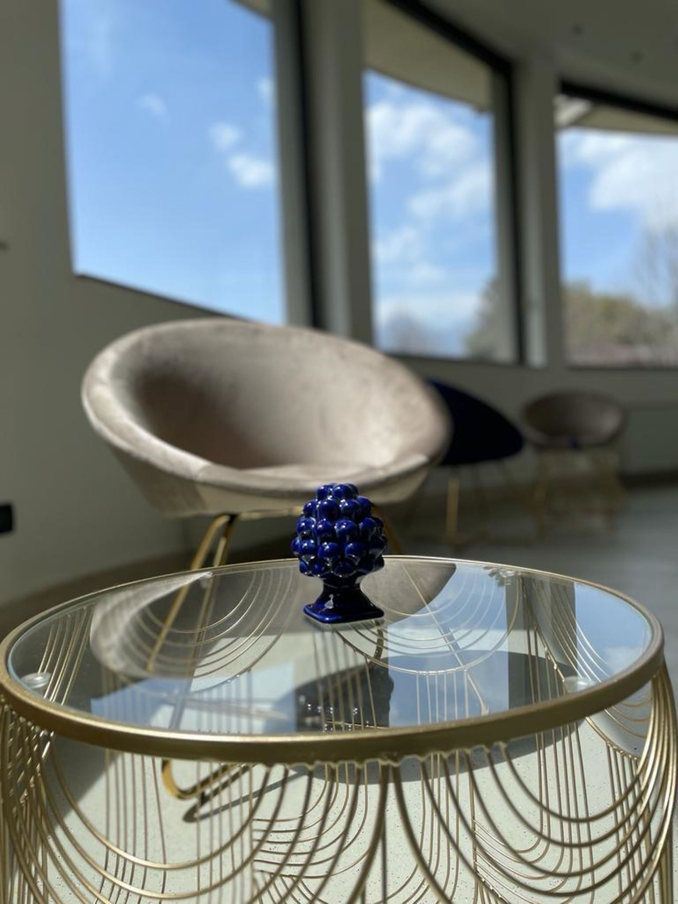 A modern interior with a glass-top table featuring a decorative blue object, a beige chair, and a view of the sky through large windows.