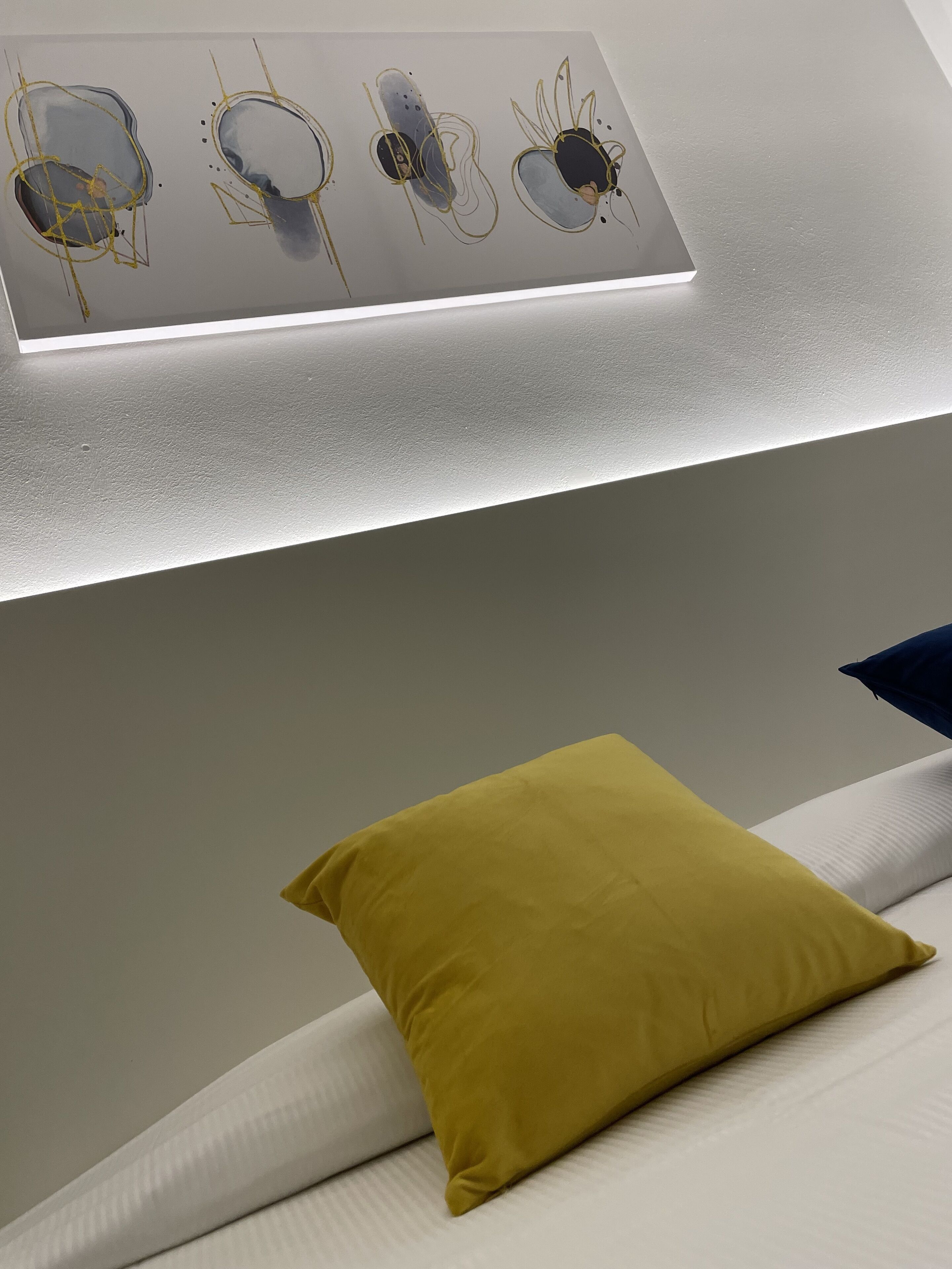 A modern room with a bed, a yellow pillow, and abstract art on the wall.