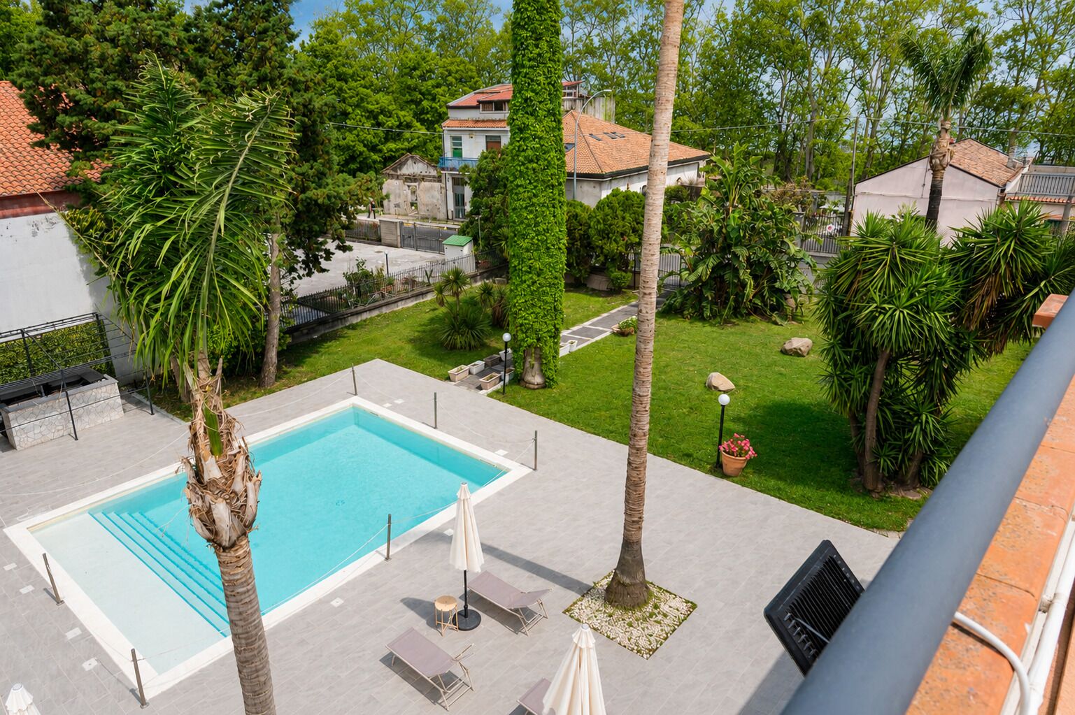 A swimming pool with lounge chairs and umbrellas, surrounded by greenery and residential buildings.