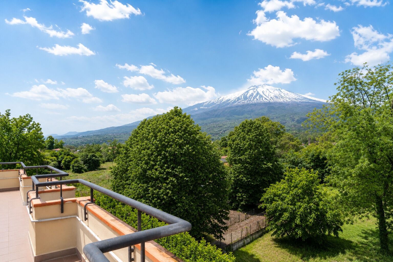 Ein Balkon mit Blick auf einen mit Schnee bedeckten Berg, üppiges Grün und einen klaren Himmel.