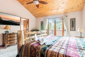 A bedroom with a wooden ceiling, a bed with a patterned blanket, a wooden headboard, a dresser, and a window with curtains.